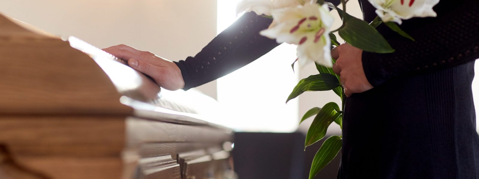 people and mourning concept - woman with white lily flowers and coffin at funeral in church